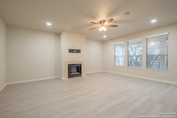 an empty room with windows chandelier fan and fireplace