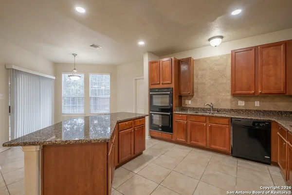 a large kitchen with granite countertop a sink and dishwasher a stove a refrigerator with wooden cabinets