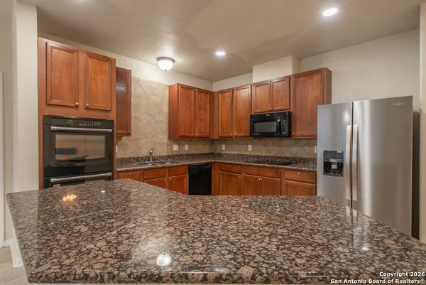 a kitchen with stainless steel appliances granite countertop a refrigerator a stove and a sink with wooden cabinets
