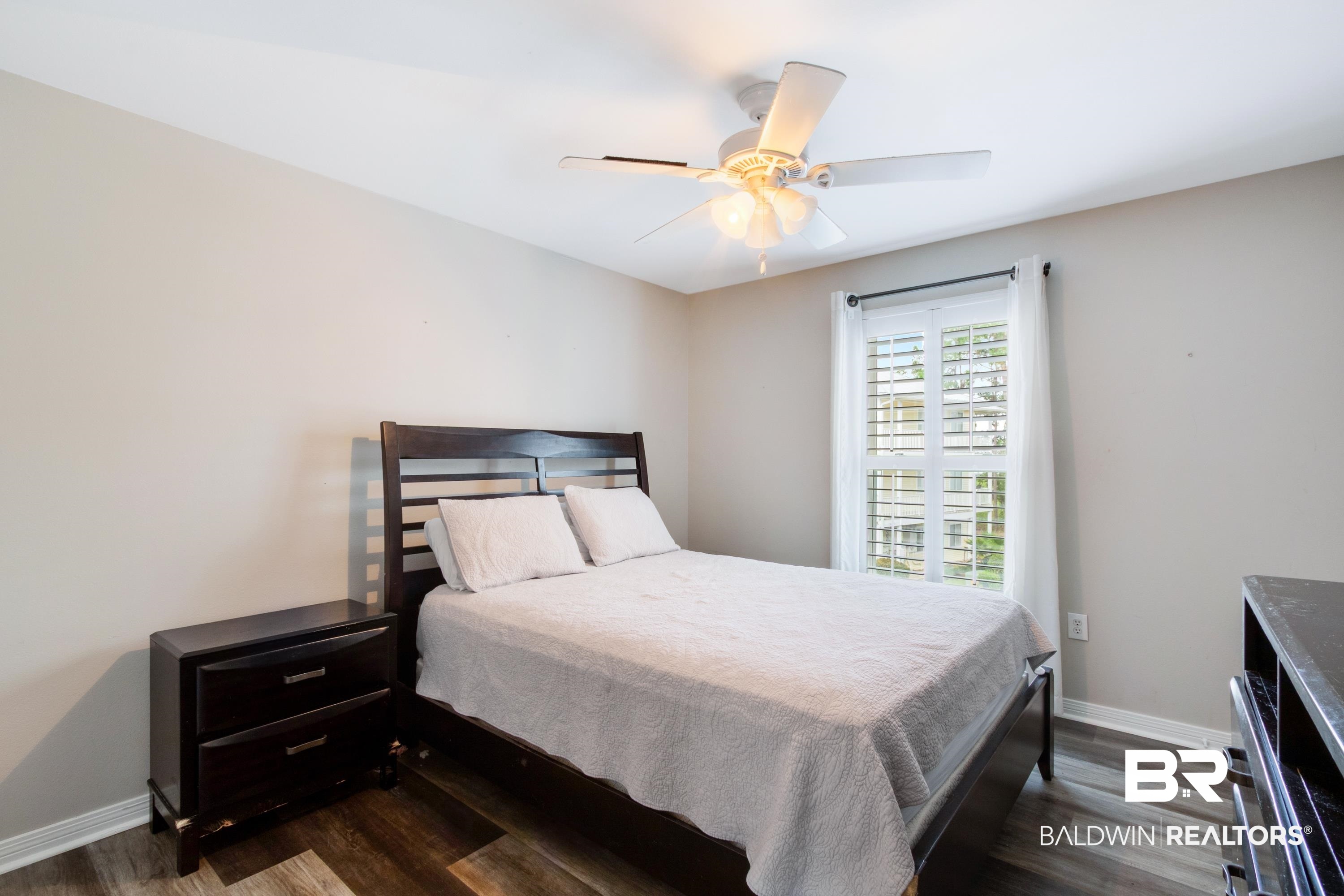 25957 Canal Road, Unit 208 Orange Beach, AL 36561 - Photo 17 of 28 Bedroom featuring wood-finish flooring, a window with plantation shutters and drapes, a ceiling fan with integrated lighting, and neutral wall tones