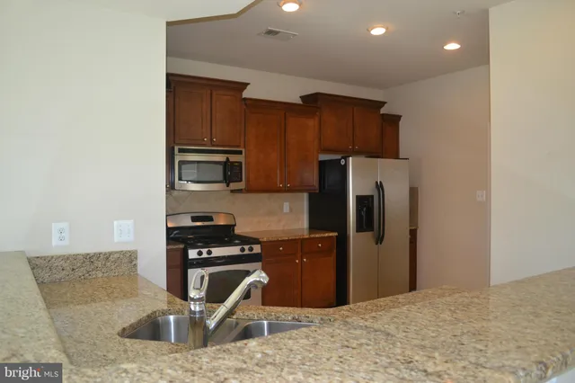 a kitchen with stainless steel appliances granite countertop a refrigerator a stove and a sink with wooden cabinets