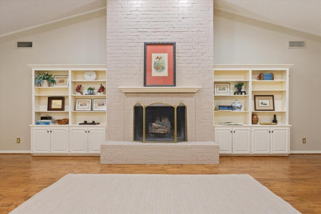 4108 Old Mill Road Waco, TX 76710 - Photo 8 of 39 Vaulted ceiling, painted brick fireplace with hearth, brass-finish fire screen, built-in shelving, and hardwood flooring