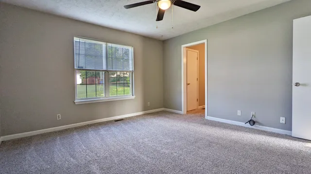 an empty room with chandelier fan and windows
