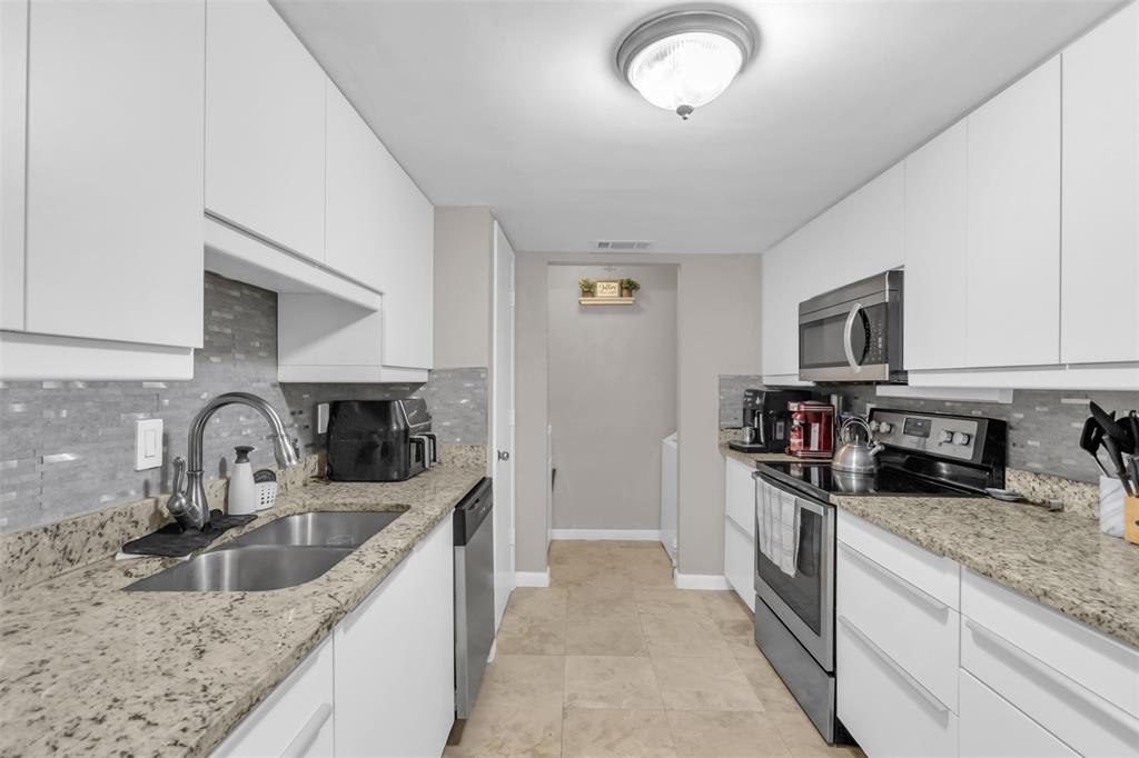 7670 Kings Ridge Road Frisco, TX 75035 - Photo 8 of 24 Kitchen with decorative backsplash, stainless steel appliances, white cabinets, light stone countertops, and modern cabinets