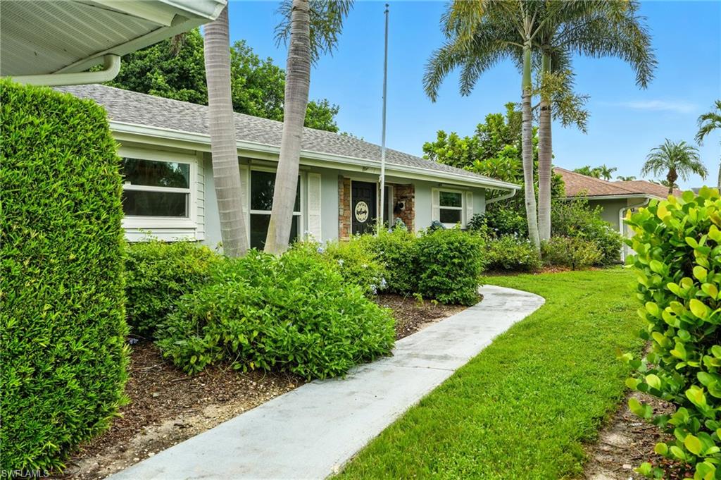 249 Pebble Beach Circle Naples, FL 34113 - Photo 4 of 45 View of exterior entry featuring a yard, a shingled roof, and stone siding