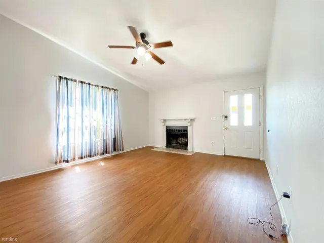an empty room with wooden floor fan and windows