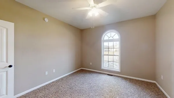 an empty room with a chandelier fan and windows