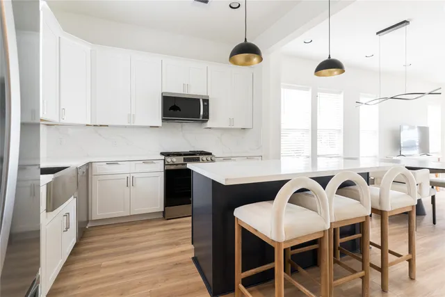 a kitchen with stainless steel appliances granite countertop a refrigerator a microwave a stove a sink dishwasher a dining table and chairs with wooden floor