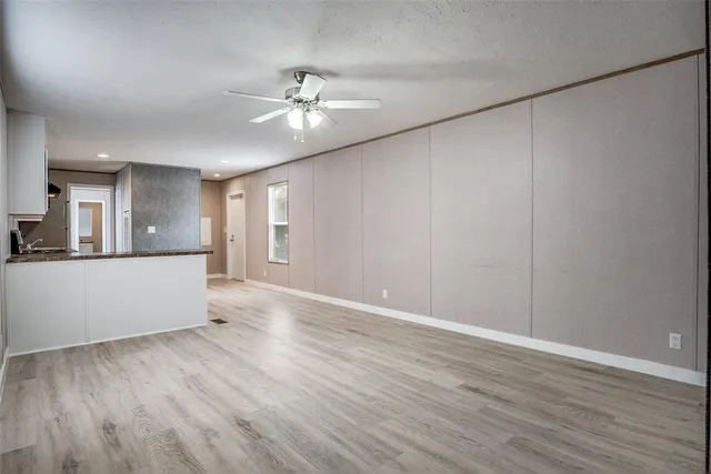 a view of an empty room with wooden floor and a kitchen