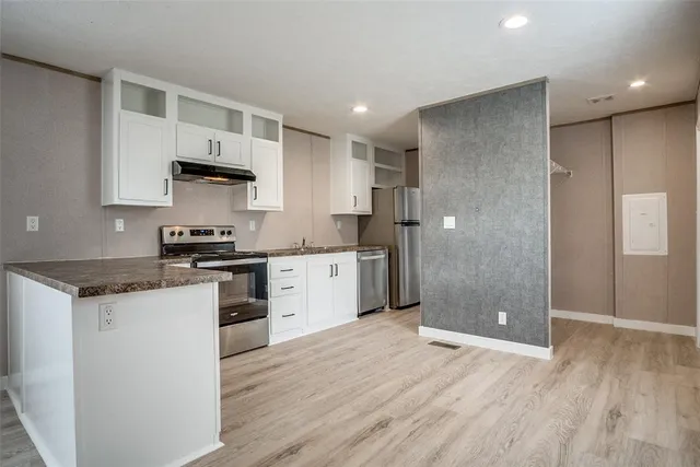 a kitchen with stainless steel appliances granite countertop a refrigerator a sink dishwasher and white cabinets with wooden floor