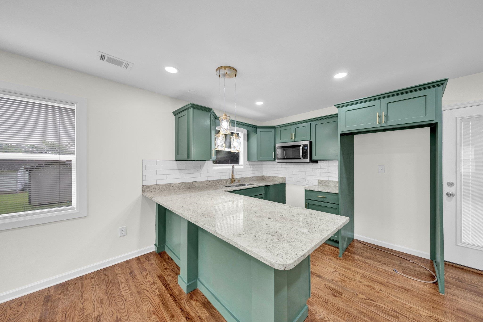 6681 Raleigh Millington Road Millington, TN 38053 - Photo 9 of 28 Kitchen featuring green cabinets, stainless steel microwave, a peninsula, decorative backsplash, and light wood-style flooring