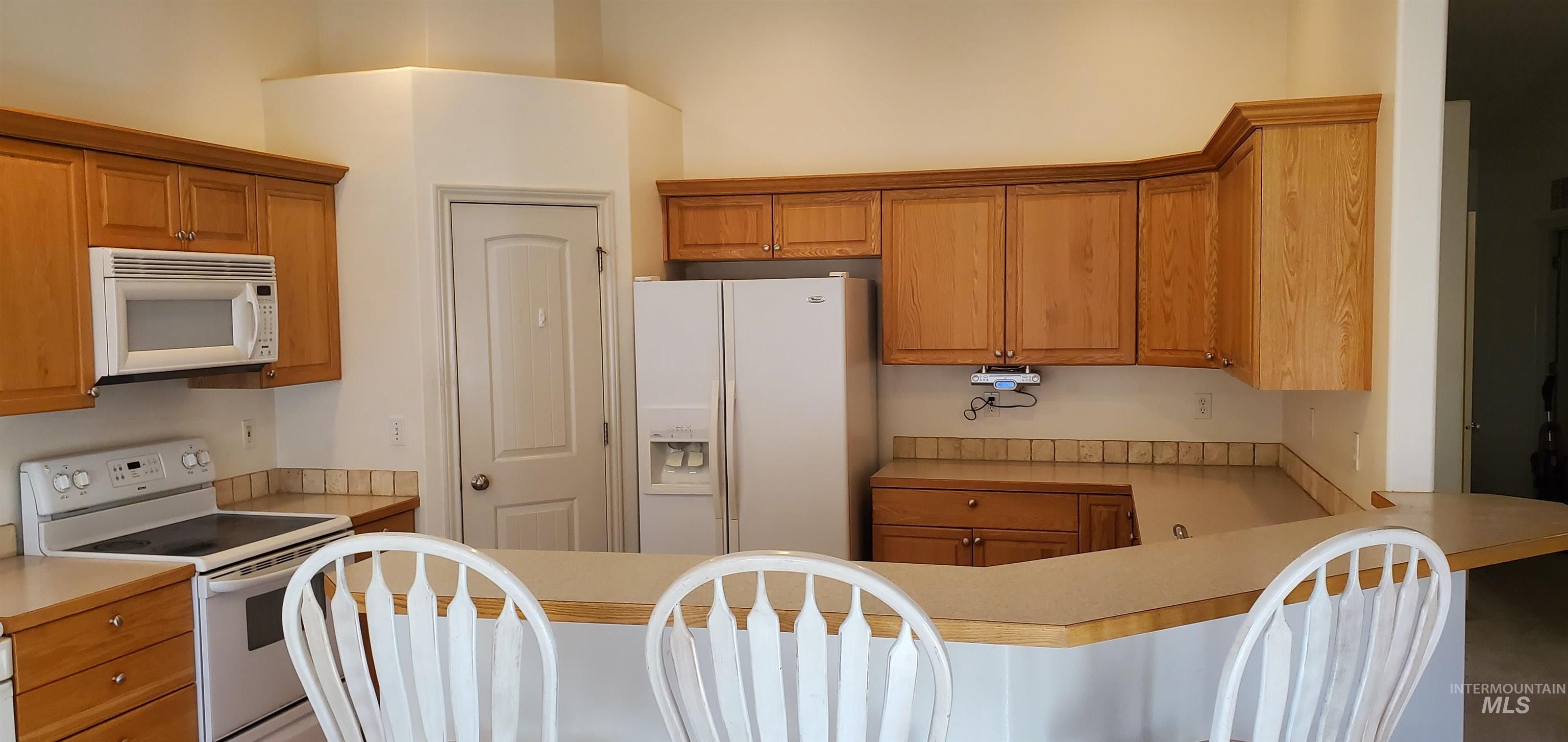 1000 North Rodeo Street Parma, ID 83660 - Photo 5 of 35 Kitchen with white appliances, light countertops, wood finish cabinets, a breakfast bar, and a peninsula