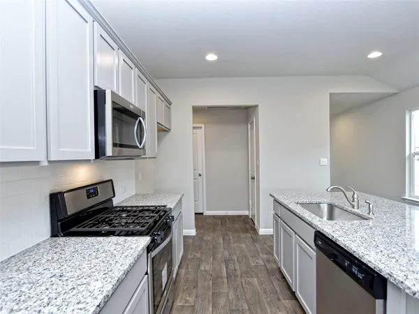 a kitchen with granite countertop a sink a stove top oven and wooden floor