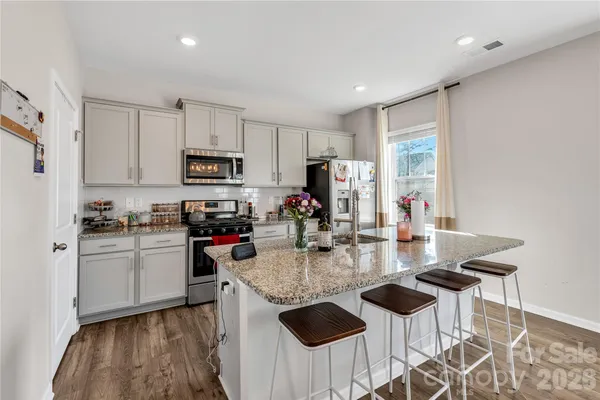 a kitchen with stainless steel appliances granite countertop a stove top oven a sink dishwasher and a refrigerator with wooden floor