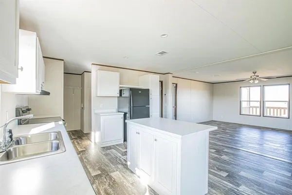 a large white kitchen with a refrigerator a sink dishwasher a stove and a window with wooden floor