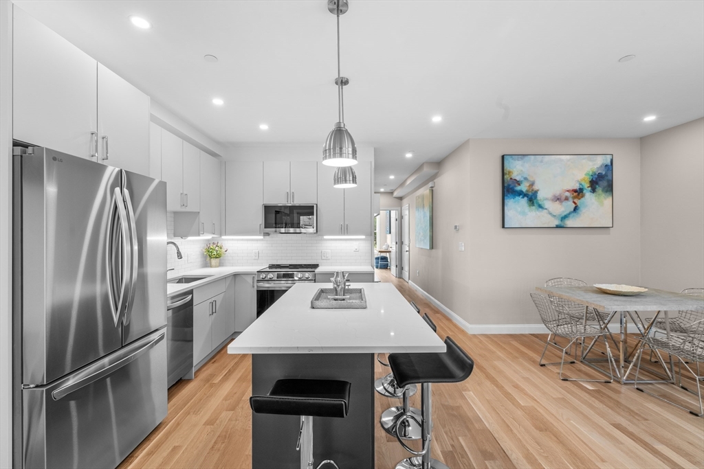 42 Waverly Street, Unit M Boston, MA 02135 - Photo 8 of 24 a kitchen with stainless steel appliances kitchen island granite countertop a refrigerator a stove a sink a dining table and chairs with wooden floor