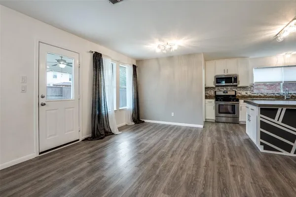 an empty room with wooden floor kitchen view and a window