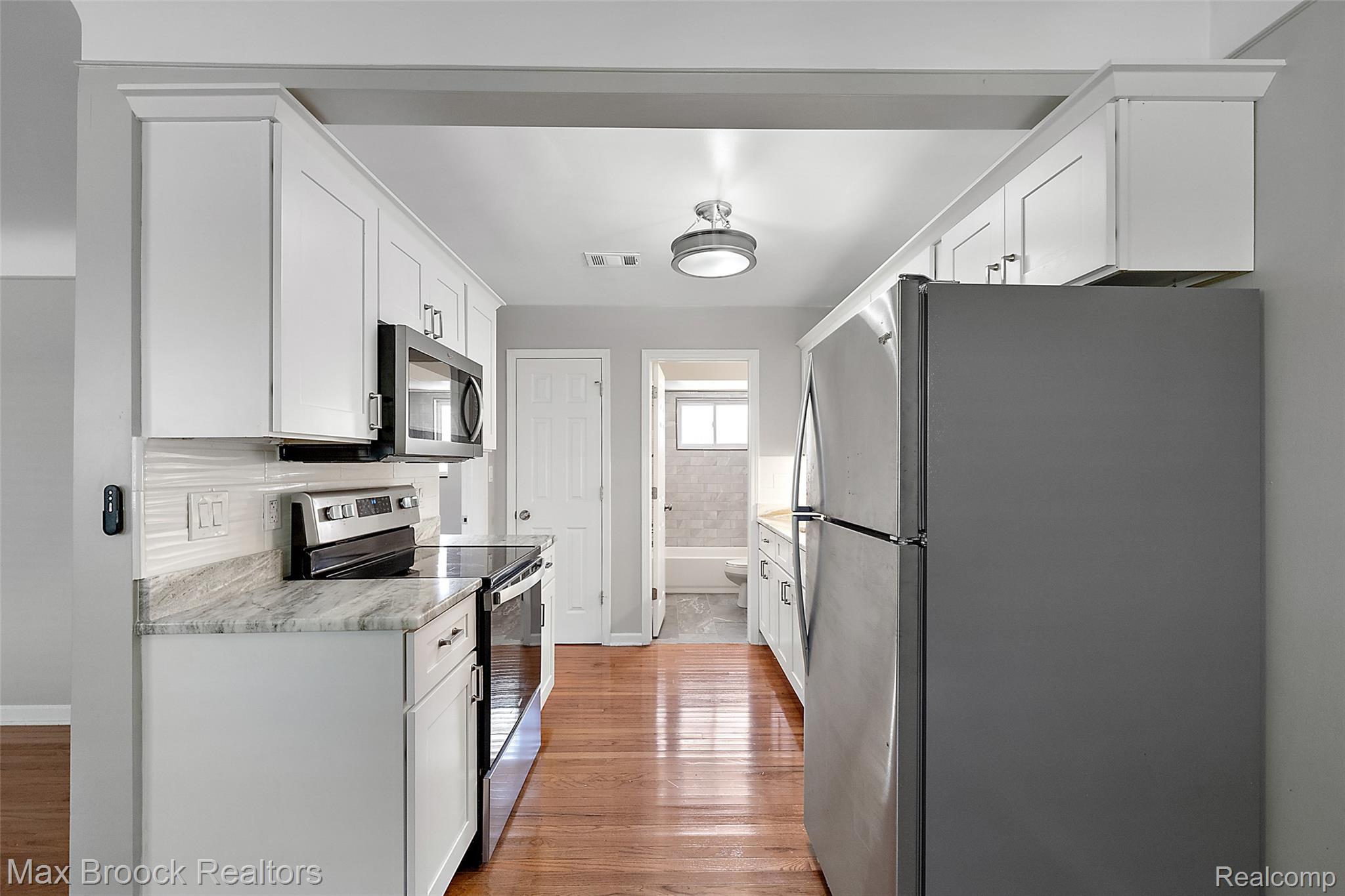 3905 Devon Road, Unit #4 Royal Oak, MI 48073 - Photo 8 of 21 Galley kitchen featuring hardwood flooring, white shaker cabinets, stainless steel appliances, light-toned countertops, and a white tile backsplash