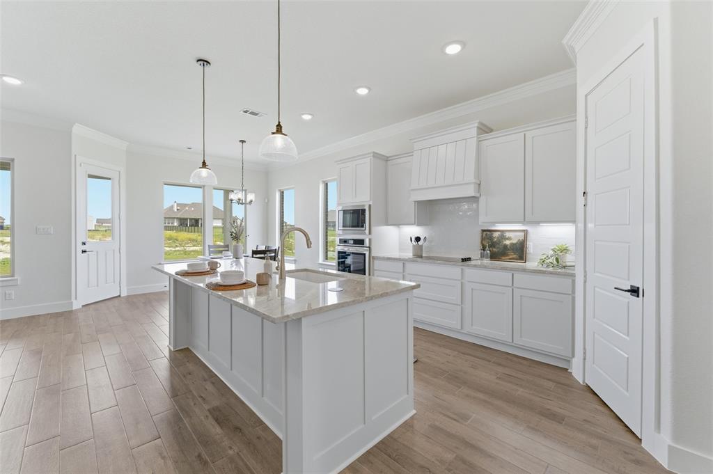 2433 Meteor Drive Krum, TX 76249 - Photo 11 of 29 Modern kitchen featuring a large central island with a sink, pendant lighting, shaker-style cabinetry, stainless steel appliances, and wood-finish flooring