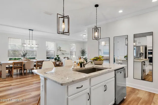 a kitchen with stainless steel appliances kitchen island granite countertop a refrigerator a sink dishwasher and white cabinets with wooden floor