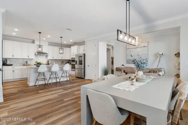 a view of a dining room and livingroom with furniture wooden floor a rug a painting and a chandelier