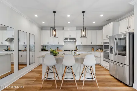 a kitchen with stainless steel appliances kitchen island granite countertop a refrigerator a stove a oven and white cabinets with wooden floor