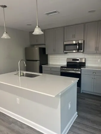 a kitchen with stainless steel appliances a sink dishwasher a stove and white cabinets with wooden floor
