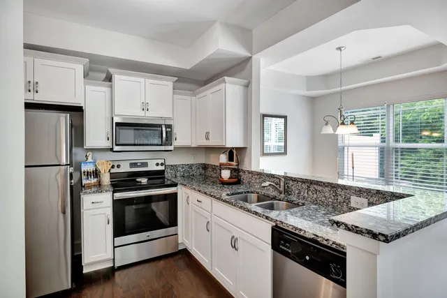 a kitchen with granite countertop white cabinets appliances and a window