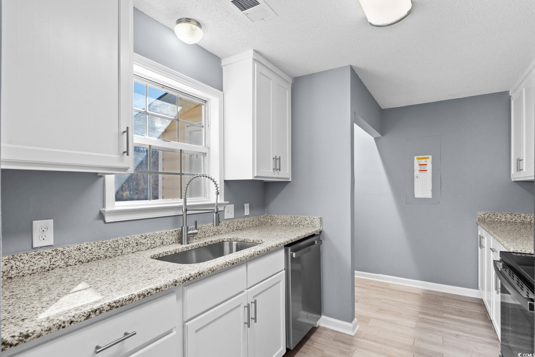 3343 New Road Conway, SC 29527 - Photo 12 of 36 Kitchen with white cabinets, light stone countertops, stainless steel appliances, light wood-style flooring, and a textured ceiling