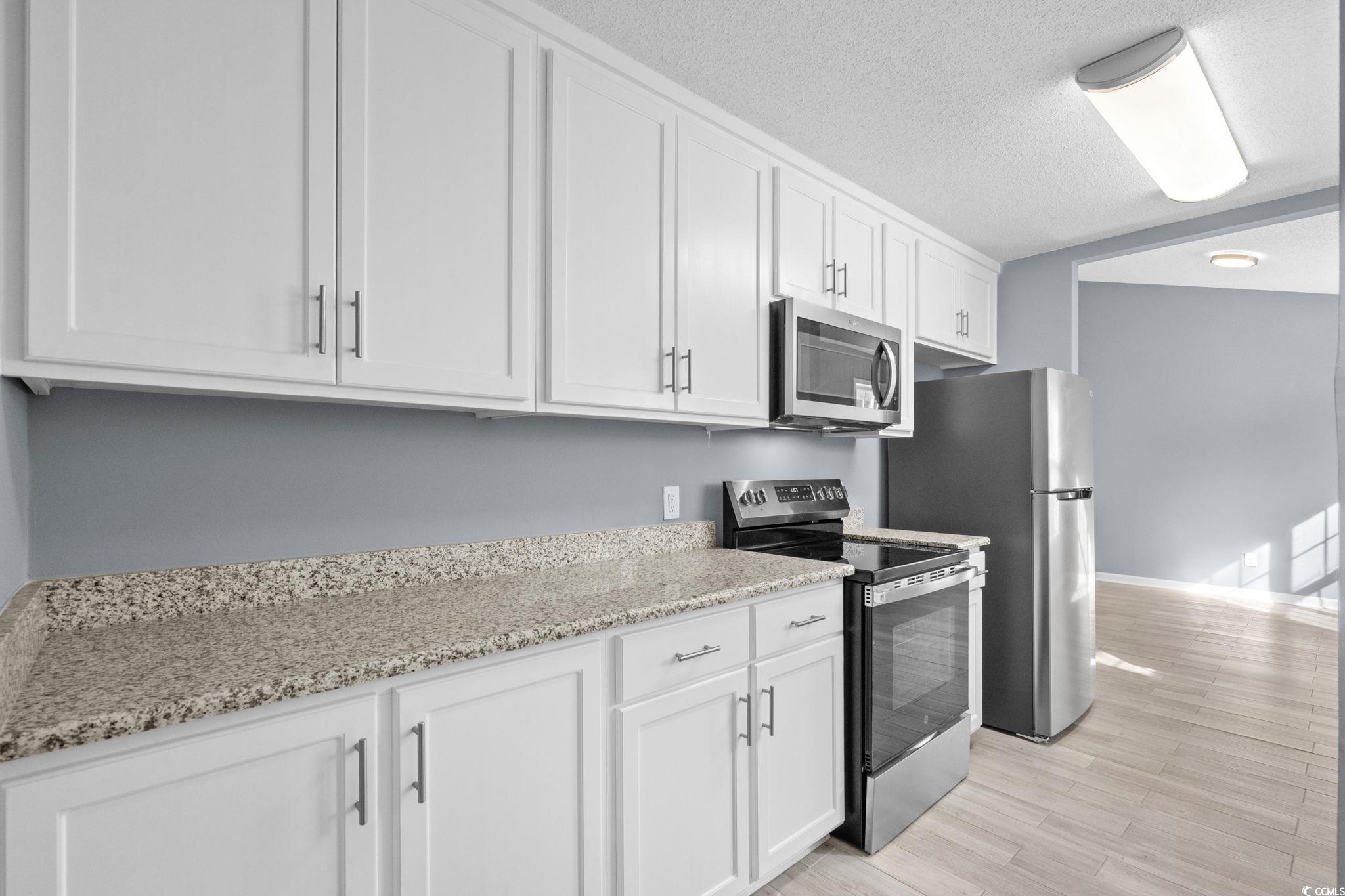 3343 New Road Conway, SC 29527 - Photo 13 of 36 Kitchen featuring stainless steel appliances, white cabinetry, light stone countertops, a textured ceiling, and light wood-style floors