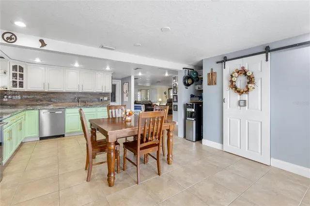 a dining area with stainless steel appliances kitchen island granite countertop a dining table chairs and a refrigerator