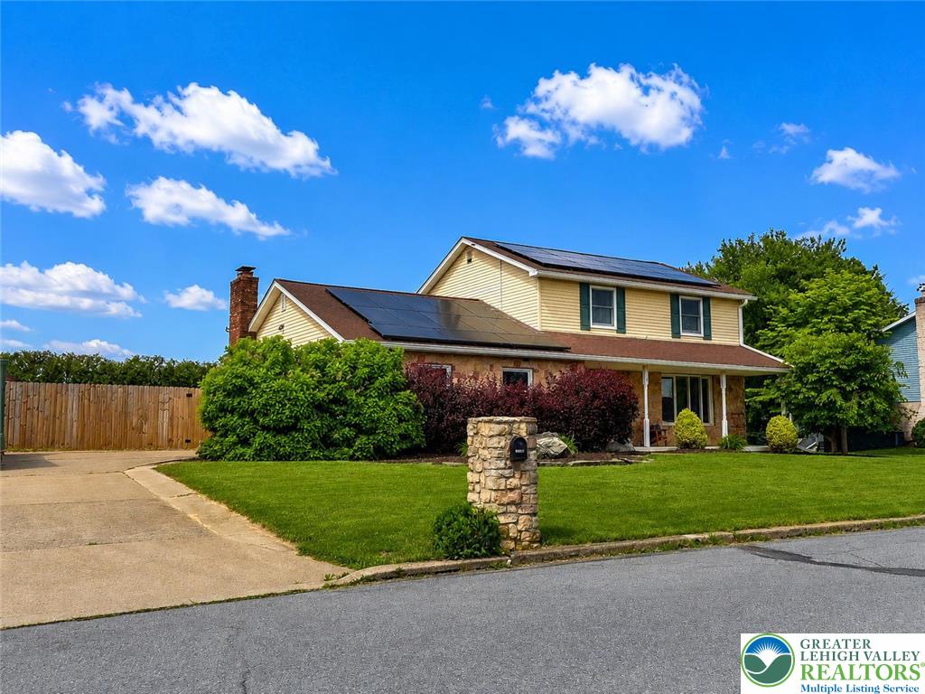 A classic two-story residence with solar panels on the roof, nestled among verdant landscaping.