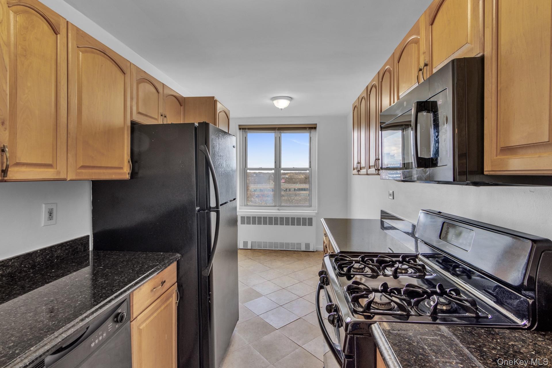 211-40 18th Avenue, Unit 6C Queens, NY 11360 - Photo 12 of 41 Kitchen featuring black appliances, radiator heating unit, light tile patterned floors, dark stone counters, and brown cabinets