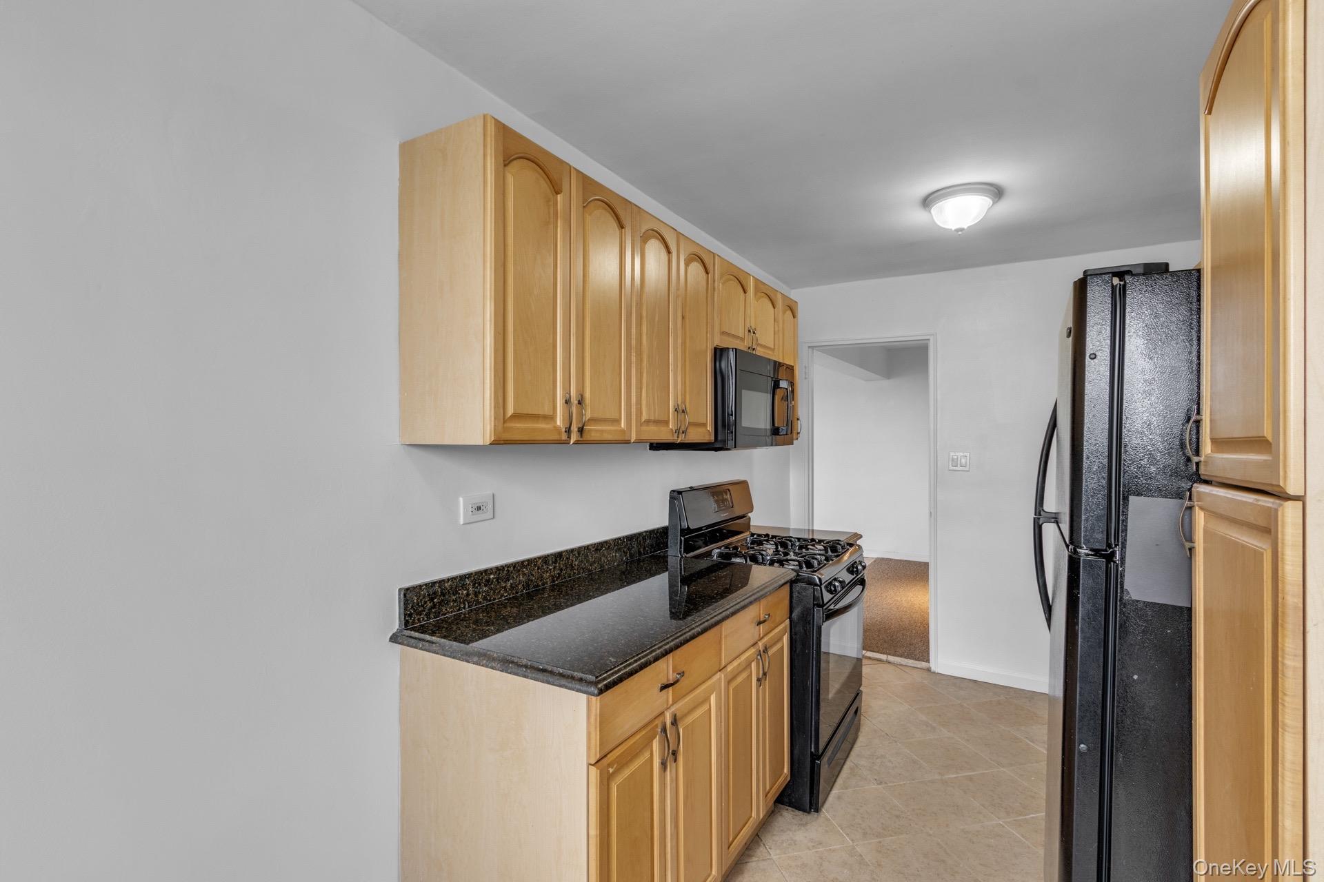 211-40 18th Avenue, Unit 6C Queens, NY 11360 - Photo 14 of 41 Kitchen with black appliances, dark stone counters, light tile patterned floors, and light brown cabinets