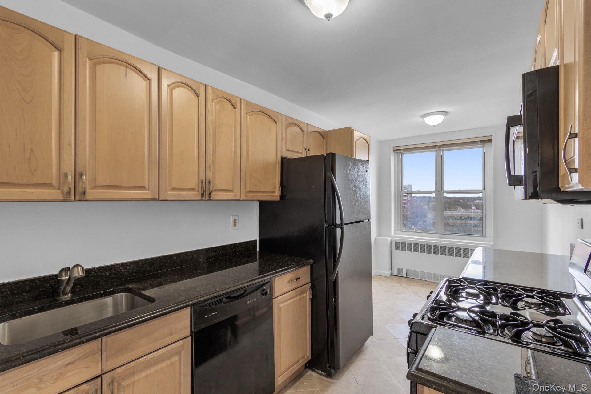 211-40 18th Avenue, Unit 6C Queens, NY 11360 - Photo 10 of 41 Kitchen with black appliances, dark stone countertops, radiator heating unit, light tile patterned floors, and light brown cabinets