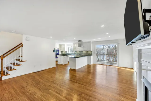 a view of an empty room with wooden floor and a kitchen