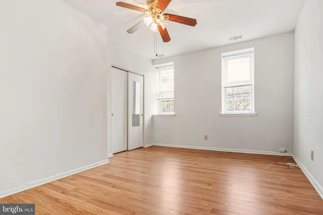 an empty room with wooden floor chandelier fan and windows