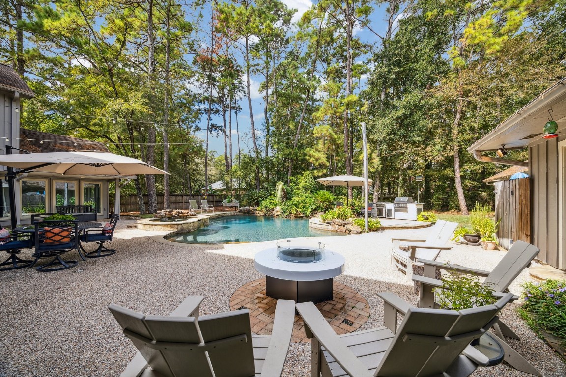 a view of a patio with table and chairs under an umbrella with barbeque grill and plants