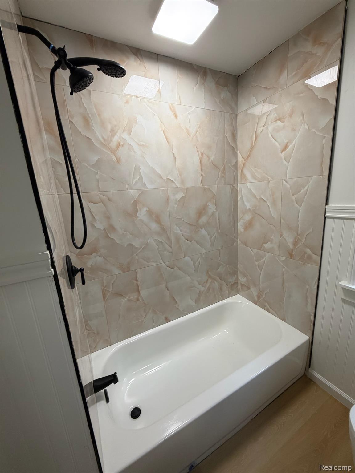 9869 Yorkshire Road Detroit, MI 48224 - Photo 5 of 14 Tub and shower combination featuring a matte black shower head and faucet, light-toned marble-look tile surround, and wainscoting