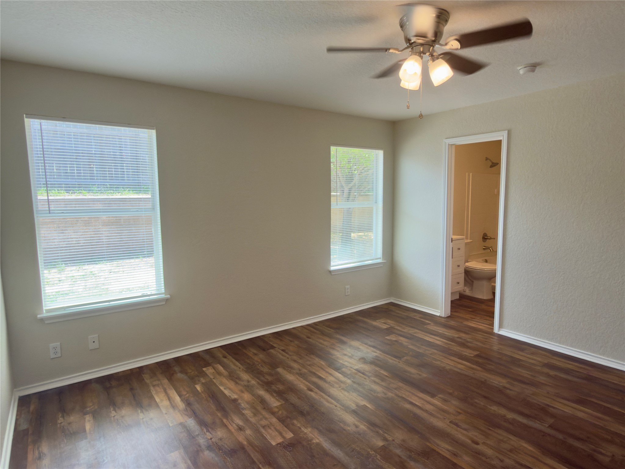 255 Myrtle Street Kyle, TX 78640 - Photo 14 of 31 Spacious room featuring wood-finish flooring, two windows with blinds, a ceiling fan with integrated lighting, and neutral wall tones
