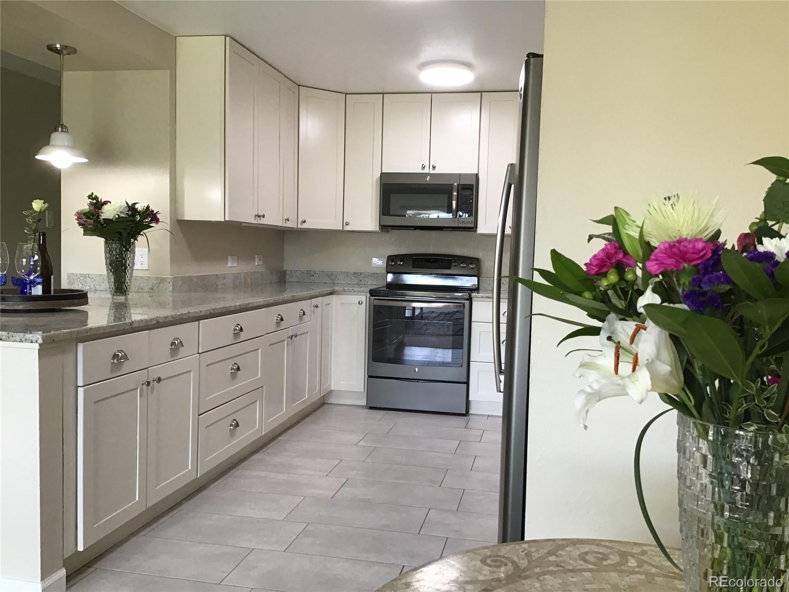 9340 Center Avenue, Unit 6B Denver, CO 80247 - Photo 10 of 40 a kitchen with stainless steel appliances kitchen island granite countertop white cabinets a potted plant a sink and a counter