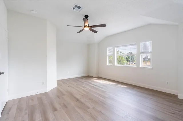 an empty room with wooden floor a ceiling fan and windows