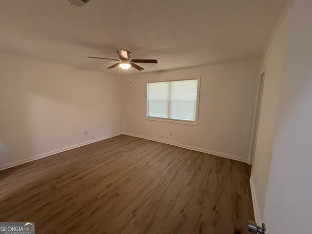 an empty room with wooden floor ceiling fan and windows