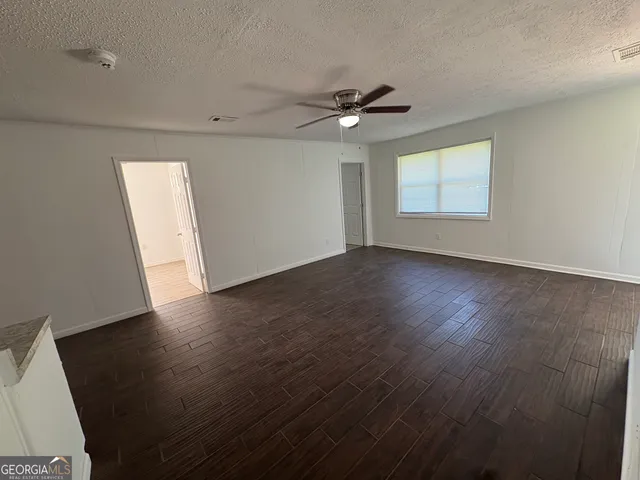 an empty room with wooden floor chandelier fan and windows