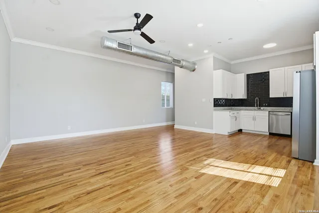 a view of empty room with wooden floor and kitchen view