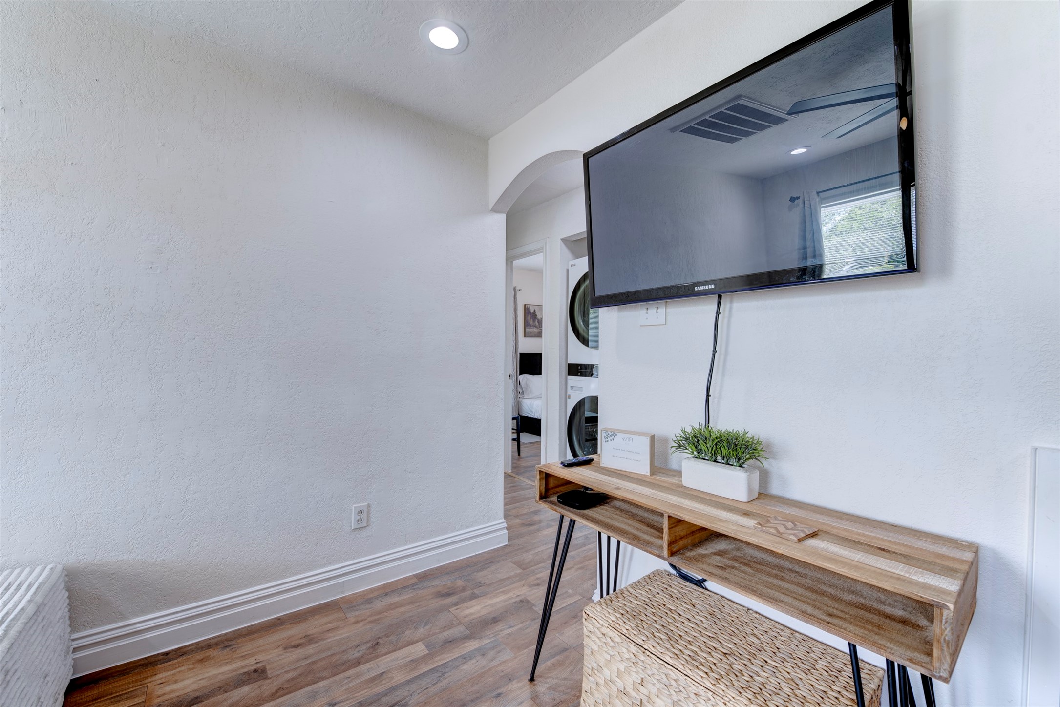 1121 Panama Street Houston, TX 77009 - Photo 26 of 35 Living room TV wall detail featuring wall-mounted Samsung flat screen TV, natural wood hairpin leg console table, recessed lighting, arched hallway leading to bedrooms and in-unit stacked laundry, and wood-look LVP flooring throughout.