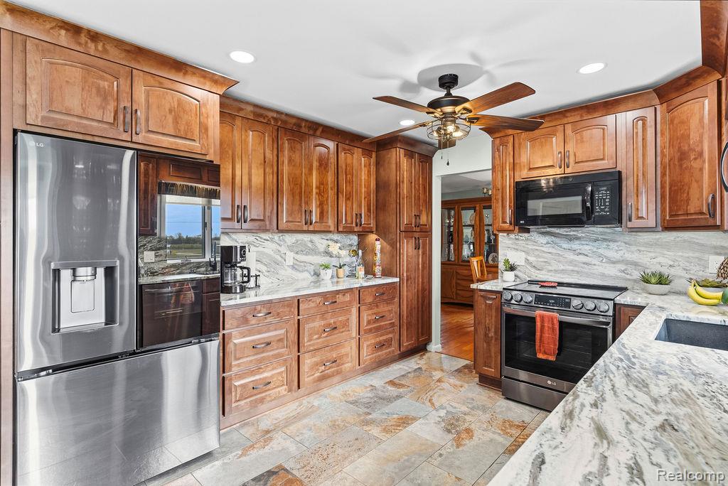 8742 Hyne Road Brighton, MI 48114 - Photo 22 of 65 Kitchen with stainless steel appliances, light stone counters, wood finish cabinetry, a ceiling fan, and decorative backsplash