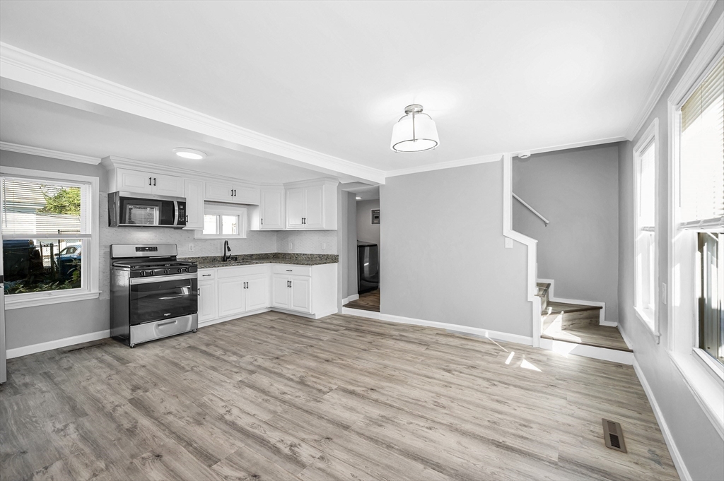 213 Prospect Street Lawrence, MA 01841 - Photo 9 of 33 a large white kitchen with granite countertop a stove top oven a sink dishwasher and a refrigerator with wooden floor