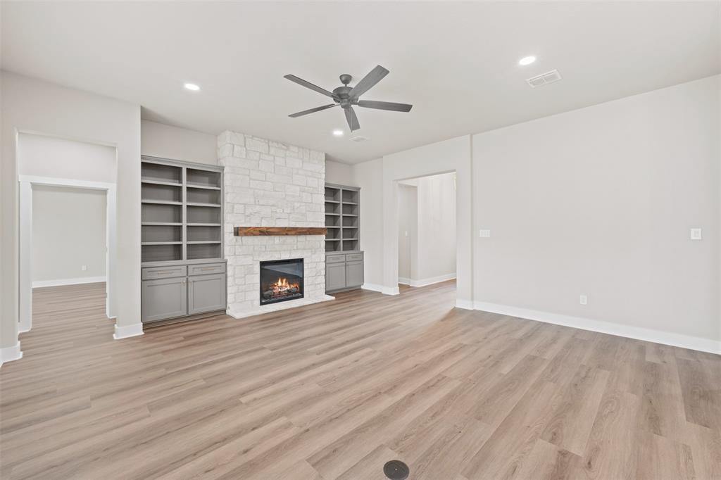 9824 Durango Trail Waco, TX 76712 - Photo 5 of 30 Spacious room featuring wood-finish flooring, a stone-clad fireplace with a wood mantel, and built-in shelving with lower cabinetry