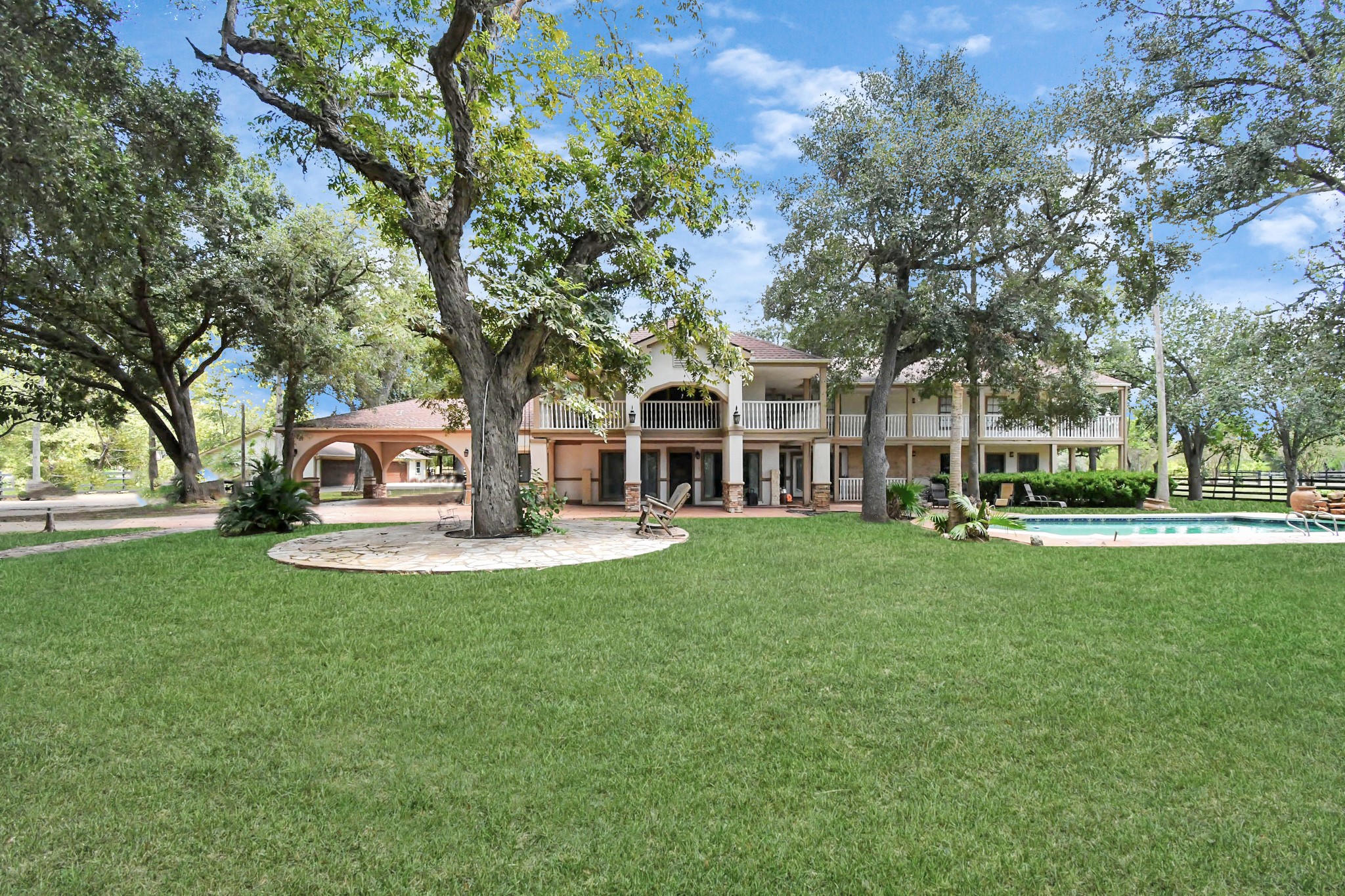 1347 Seidel Road Brookshire, TX 77423 - Photo 5 of 50 Sprawling elegance meets natural charm — this beautiful estate showcases a two-story wraparound veranda, resort-style pool, and shaded relaxation areas, all nestled within a serene, tree-filled landscape.